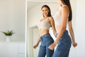 A young woman looking at herself in the mirror, reflecting on her progress at a Semaglutide Weight Loss Clinic in Boynton Beach.