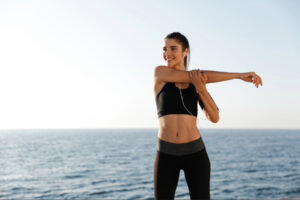 Woman performing outdoor dynamic stretching by the ocean, symbolizing active lifestyle integration, metabolic health optimization, and the supportive role of movement in neurohormonal balance and semaglutide-guided wellness.